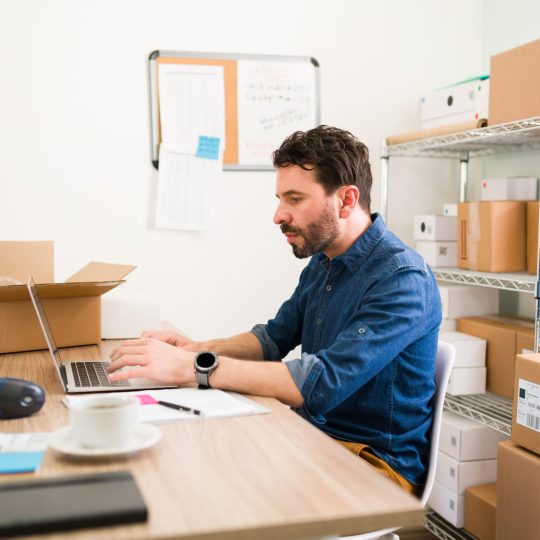 Good-looking man typing on a laptop and posting on his online shop the new products of his business startup