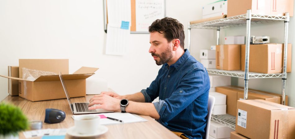 Good-looking man typing on a laptop and posting on his online shop the new products of his business startup